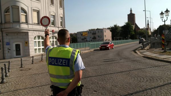 Ein Polizeibeamter bei einer Grenzkontrolle. Ein Polizeibeamter hat die Polizeikelle erhoben um ein Fahrzeug anzuhalten.