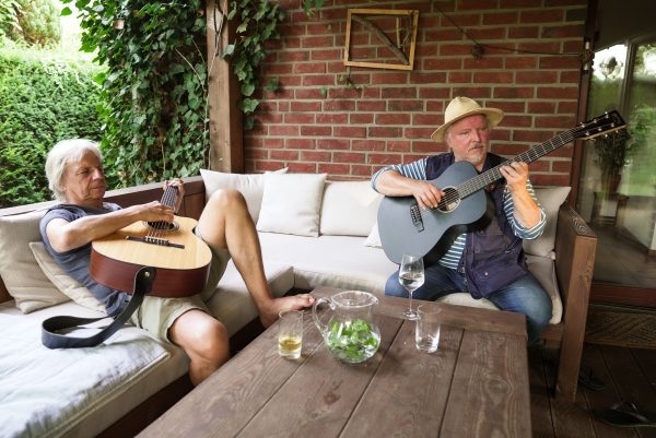 Andreas Dresen und Axel Prahl sitzen auf einem Sofa. Beide halten eine Gitarre in der Hand musizieren gemeinsam.