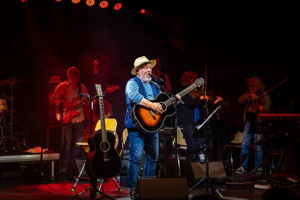 Axel Prahl steht mit Gitarre auf der Bühne und singt.