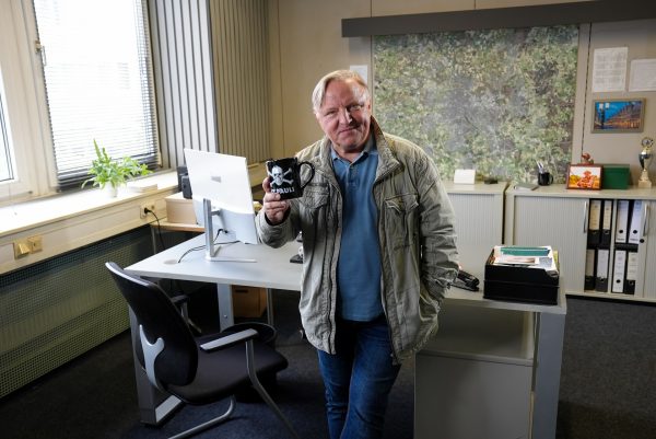 Axel Prahl steht vor einem Schreibtisch am Set des Tatort Münster. Er blickt in die Kamera und hält eine schwarze Tasse mit St. Pauli Logo in der Hand.