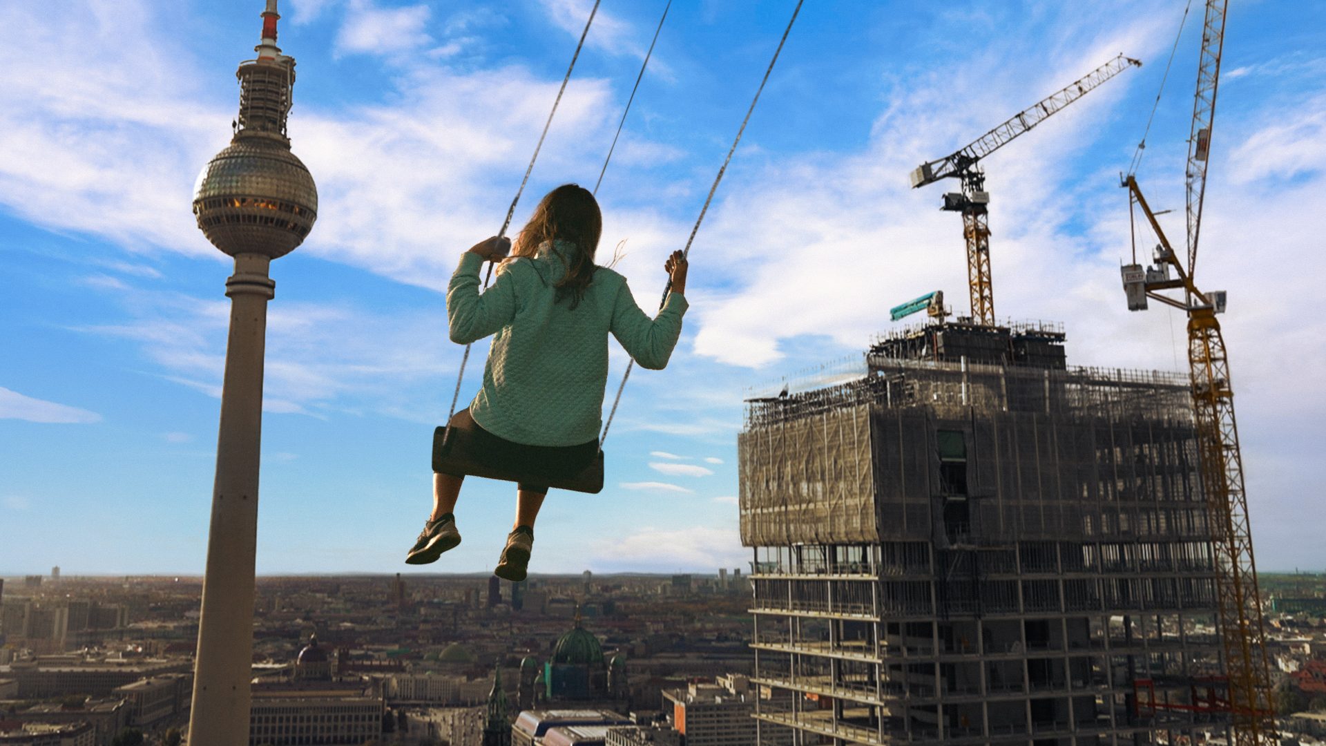 Frau schwingt auf der Highswing Schaukel hoch über dem Alexanderplatz, im Hintergrund ist der Alex und ein Hochhaus zu sehen.