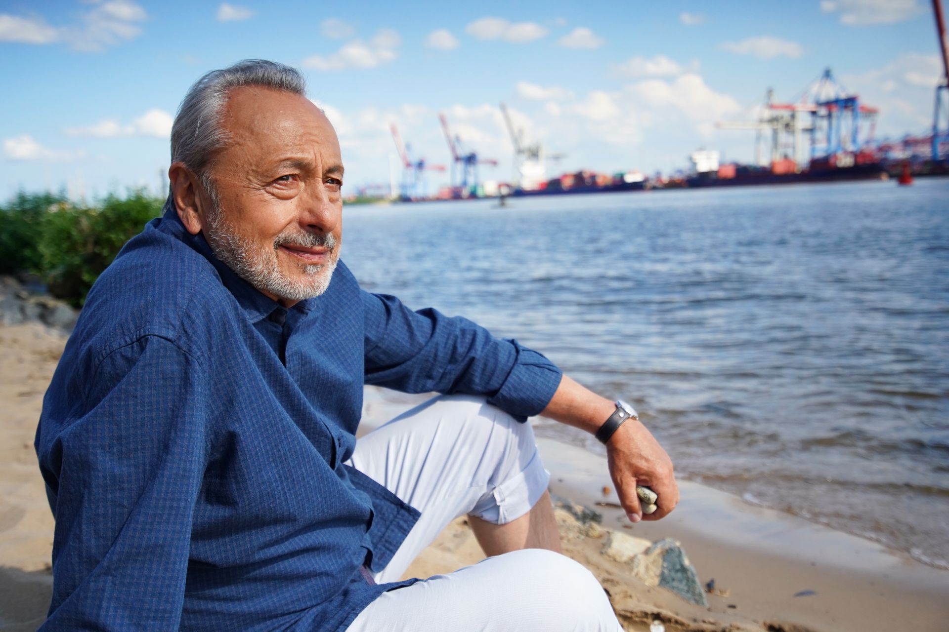 Wolfgang Stumph sitzt am Elbstrand und blickt auf die Elbe.